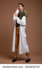 Fashion Photo Of A Beautiful Elegant Young Asian Woman In A Pretty Beige Leather Pants, White Long Cardigan, Green T-shirt, Belt Posing Over Brown Coffee Background. Studio Shot. Portrait