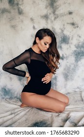 fashion photo of beautiful pregnant woman with dark hair in elegant clothes posing in studio