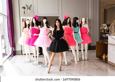 fashion photo of beautiful sexy woman with dark hair in luxurious dress posing in decorated room with mannequins in dresses