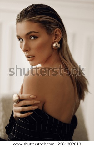 fashion photo of beautiful woman with blond hair in elegant clothes with accessories posing in hotel room