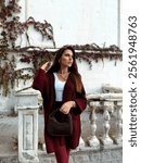 fashion photo of beautiful woman with dark hair in elegant burgundy outfit with tights walking on the street