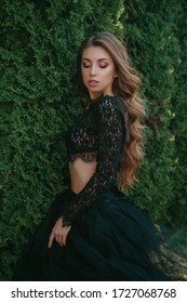 Fashion Photo Of Beautiful Young Woman With Long Curly Hair In Elegant Black Dress. Art Work Of Romantic Woman. Pretty Tenderness Model. Dress With A Trailer And Lace Sleeves. Outdoor Portrait