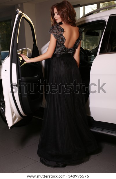 fashion photo of gorgeous\
woman with long dark hair wears luxurious dress,posing beside white\
car  