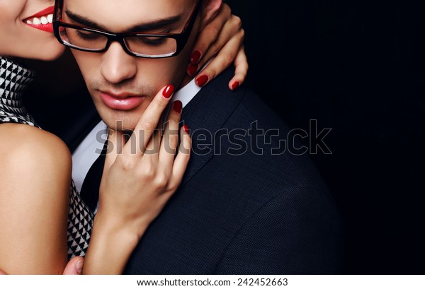 Fashion photo of office romance of sexy lovers,pretty\
blond woman with watch,red lipstick,and handsome brunette\
businessman wearing in suit,tie,glasses,they are hugging and\
kissing on Valentine\'s\
day