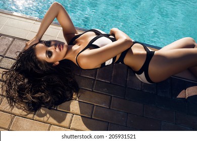 fashion photo of sexy beautiful girl with long curly hair in black and white swimsuit  relaxing beside a swimming pool