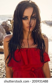 fashion photo of sexy glamour model with long dark hair in elegant red dress posing on beach with  sea on background