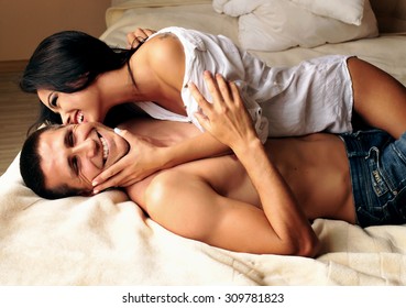 Fashion photo of two young beautiful brunet lovers relaxing and smiling at the hotel on a bed