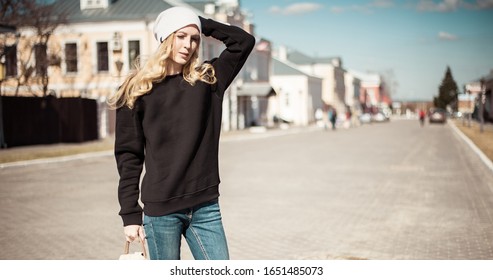 Fashion photo of a young beautiful woman in jeans, a black sweatshirt, a white knitted hat with a backpack in her hand on the street of a European city - Shutterstock ID 1651485073