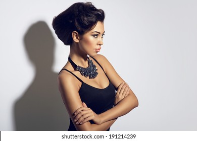 Fashion photo of young lady with nice hair style in elegant black dress, big necklace