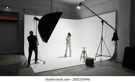 Fashion photography in a photo studio. Professional male photographer taking pictures of beautiful woman model on camera, backstage - Powered by Shutterstock