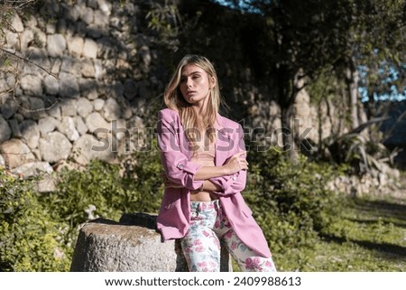Fashion Photography: Woman standing in a rustic house with green background, posing for the camera. E-commerce photoshoot. Tanned skin and blond hair. Lifestyle 