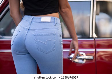 fashion picture with female booty and skinny blue jeans with place for logo, stand near red retro car hold on 
car door handle. 