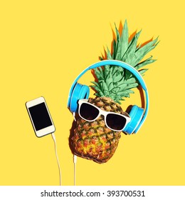 Fashion pineapple with sunglasses and headphones listens to music on smartphone over yellow background