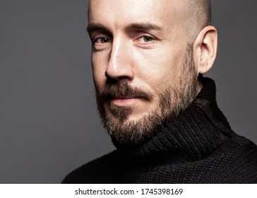 Modeportrait eines 40-jährigen Mannes, der über einem hellgrauen Hintergrund in einem schwarzen Pullover steht. Mach zu. Klassischer Stil. Bald rasierte den Kopf. Kopieren von Speicherplatz. Studio-Aufnahme