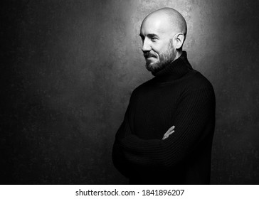 Fashion Portrait Of A 40-year-old Man Standing Over A Light Gray Background In A Black Sweater. Close Up. Classic Style. Bald Shaved Head. Copy-space. Studio Shot