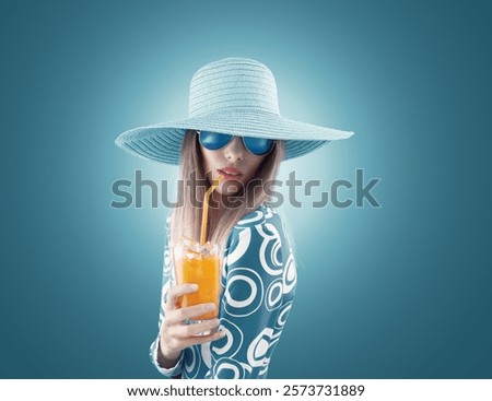 Fashion portrait of beautiful young blonde woman wearing sunglasses and summer hat, drinking a refreshing orange juice cocktail, isolated on blue background. For magazine cover or advertising poster