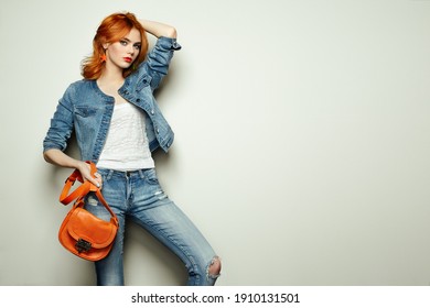 Fashion Portrait Of Beautiful Young Woman With Red Hair. Girl In Blouse And Jeans. Jewelry And Hairstyle. Girl With Handbag