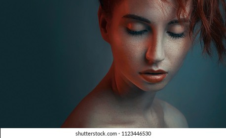 Fashion Portrait In Color Lighting Of Beautiful Red-haired Girl Face Closeup, On Dark Blue Background