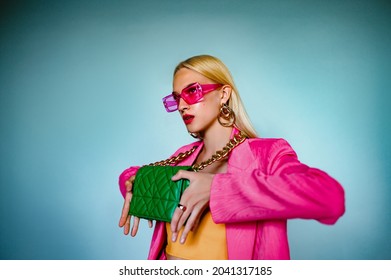 Fashion portrait of confident woman holding trendy green quilted leather bag with chunky chain. Model wearing pink sunglasses, blazer. Accessories advertising conception. Copy, empty space for text