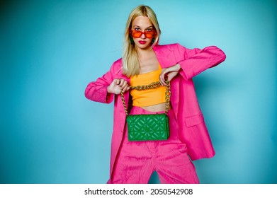 Fashion portrait of confident woman wearing trendy summer pink fuchsia color suit, orange sunglasses, holding green quilted faux leather bag, posing in studio, on blue background. Copy, empty space
 - Shutterstock ID 2050542908