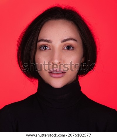 Fashion portrait of a dark-eyed beautiful young woman wearing black turtleneck on red background