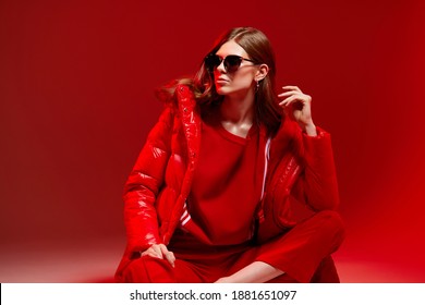 Fashion Portrait Of Elegant Trendy Woman In Red Down Jacket. Neon Light, Sunglasses, Studio Shot