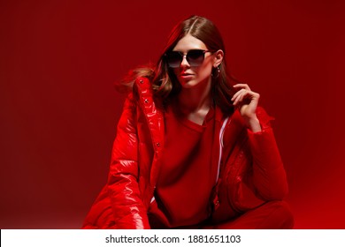 Fashion Portrait Of Elegant Trendy Woman In Red Down Jacket. Neon Light, Sunglasses, Studio Shot