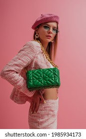 Fashion Portrait Of Elegant Woman Wearing Pink Beret, Tweed Suit, Trendy Sunglasses, With Green Quilted Bag. Studio Portrait
