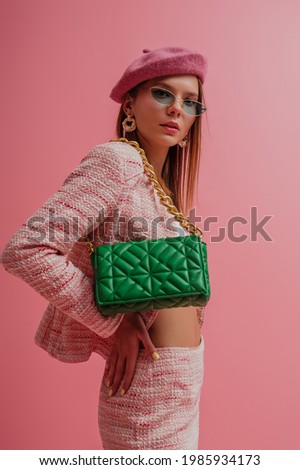 Fashion portrait of elegant woman wearing pink beret, tweed suit, trendy sunglasses, with green quilted bag. Studio portrait