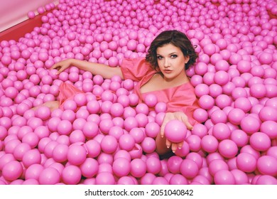 Fashion Portrait Of Happy Young Woman Playing In A Ball Pit, Wearing Pink Dress