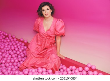 Fashion Portrait Of Happy Young Woman Playing In A Ball Pit, Wearing Pink Dress