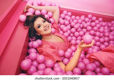 Fashion Portrait Of Happy Young Woman Playing In A Ball Pit, Wearing Pink Dress