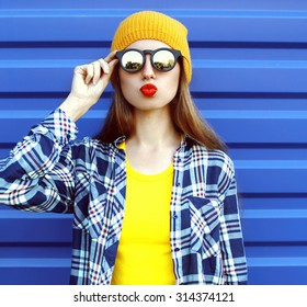 Fashion Portrait Of Hipster Cool Girl In Sunglasses And Colorful Clothes Having Fun Over Blue Background