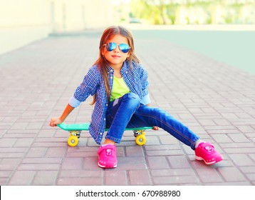 Fashion portrait little girl child sitting on skateboard in the city