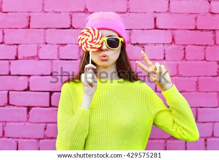 Fashion portrait pretty cool girl with lollipop having fun over colorful pink background