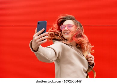 Fashion portrait of pretty smiling hipster woman in sunglasses with smartphone against the colorful orange wall
