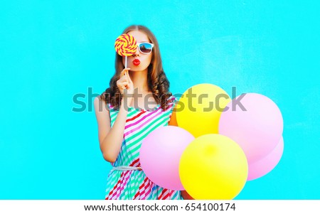 Fashion portrait pretty young woman with an air balloons, lollipop candy on a colorful blue background