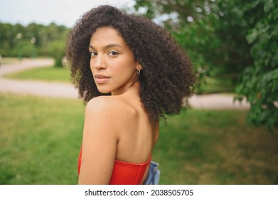 Fashion portrait of sensual attractive young naturally beautiful African American woman with afro black hair in red corset dress posing in nature parkland in green foliage