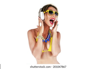 Fashion portrait of sexy beautiful happy woman listening music at her big stylish white earphones, dancing and singing. Wearing yellow bikini sunglasses and bright accessorizes.