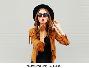 Fashion portrait woman model blowing red lips sends air sweet kiss wearing black hat, sunglasses over urban grey background