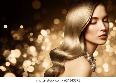 Fashion portrait of young caucasian model with gold jewelry on golden background. Beautiful blonde woman with long shiny hair. Glamour trendy accessories and hairstyle.