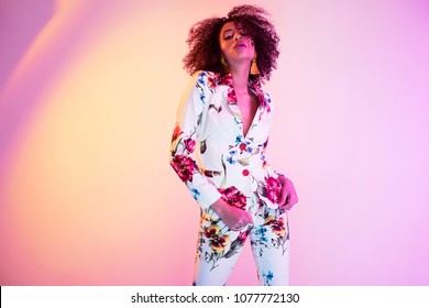 Fashion portrait of young elegant woman in nice clothes. Colored background, neon lights, studio shot. Amazing afro hair