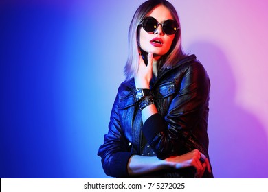 Fashion Portrait Of Young Elegant Woman In Sunglasses. Black Leather Jacket, Colored Background, Studio Shot