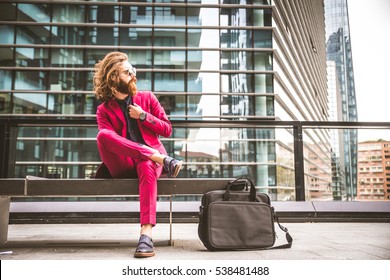 Fashion Portrait Of A Young Hipster Man Sitting On A Bench Outdoors With A Red Formal Suit - Unusual Businessman Going To Work