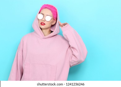 Fashion portrait of young hipster woman in pink hoody. Short pink hair, sunglasses, red lips, turquoise background - Powered by Shutterstock