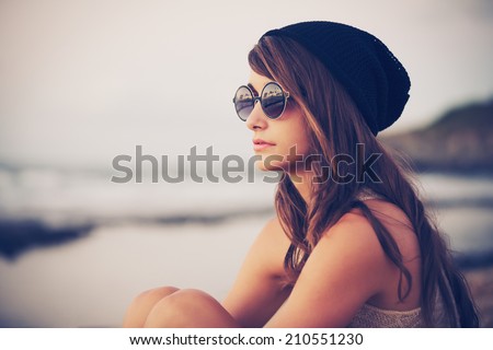 Fashion portrait of young hipster woman with hat and sunglasses on the beach at sunset, retro style color tones