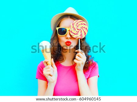 Fashion portrait young woman making an air kiss with lollipop and ice cream over colorful blue background