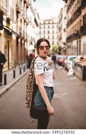 Fashion portrait of young woman smiling and wearing trendy animal, leopard print faux fur coat, fashion sunglasses, posing in Madrid city