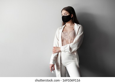Fashion portrait of young woman wearing a face mask, looking at camera, use antiseptic, isolated on gray background. Flu epidemic, dust allergy,  protection against virus. Corona virus. COVID-19.