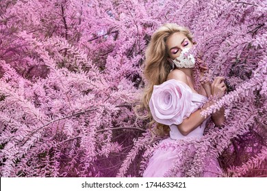 Fashion portrait of young woman wearing a face mask and pink clothes, in a flowering garden.Pandemic, virus, coronavirus, Covid-19 masked girl. Spring and summer fashion, model in a mask. - Powered by Shutterstock